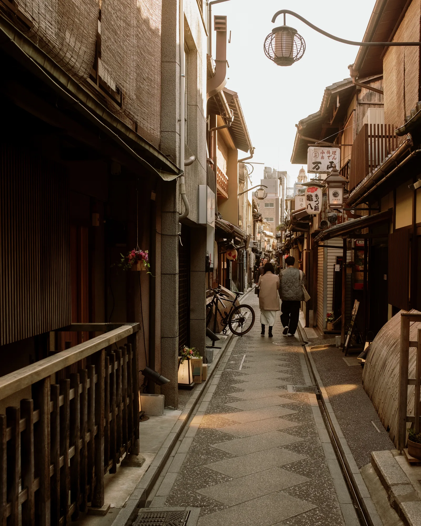 Narrow Kyoto alley with a diamond-patterned path, wooden facades and a hanging lamp