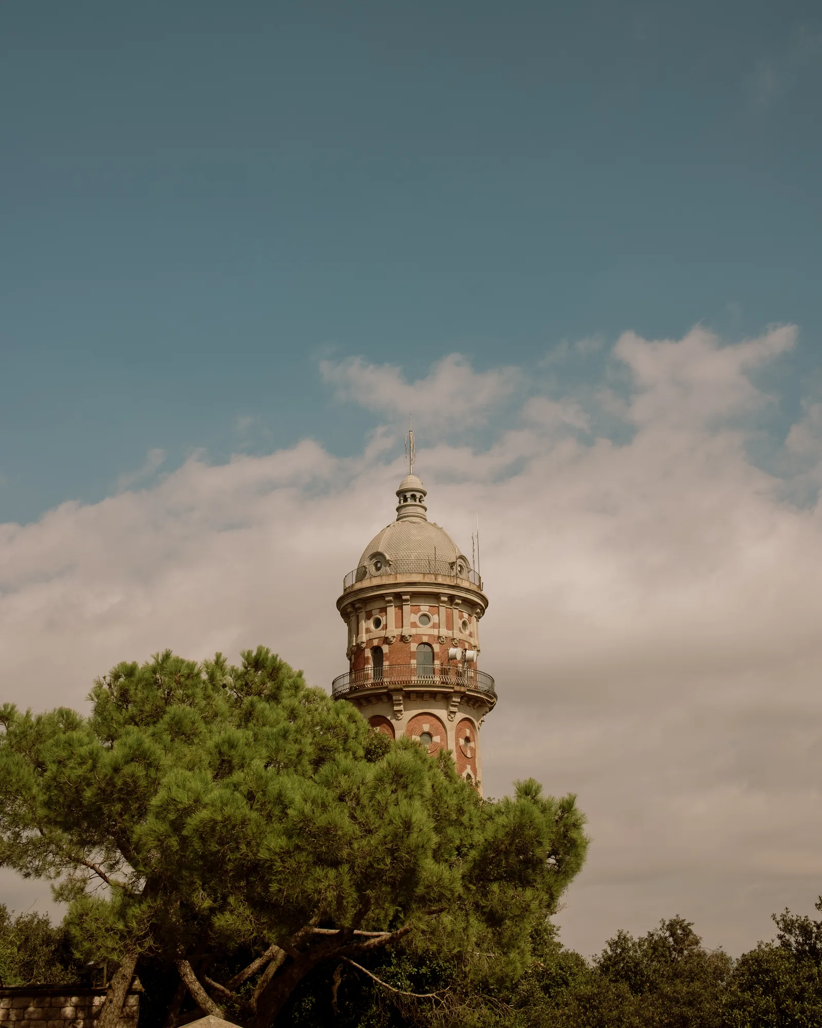 Brick and tile tower with a domed top rising above pine trees under a blue sky, Barcelona