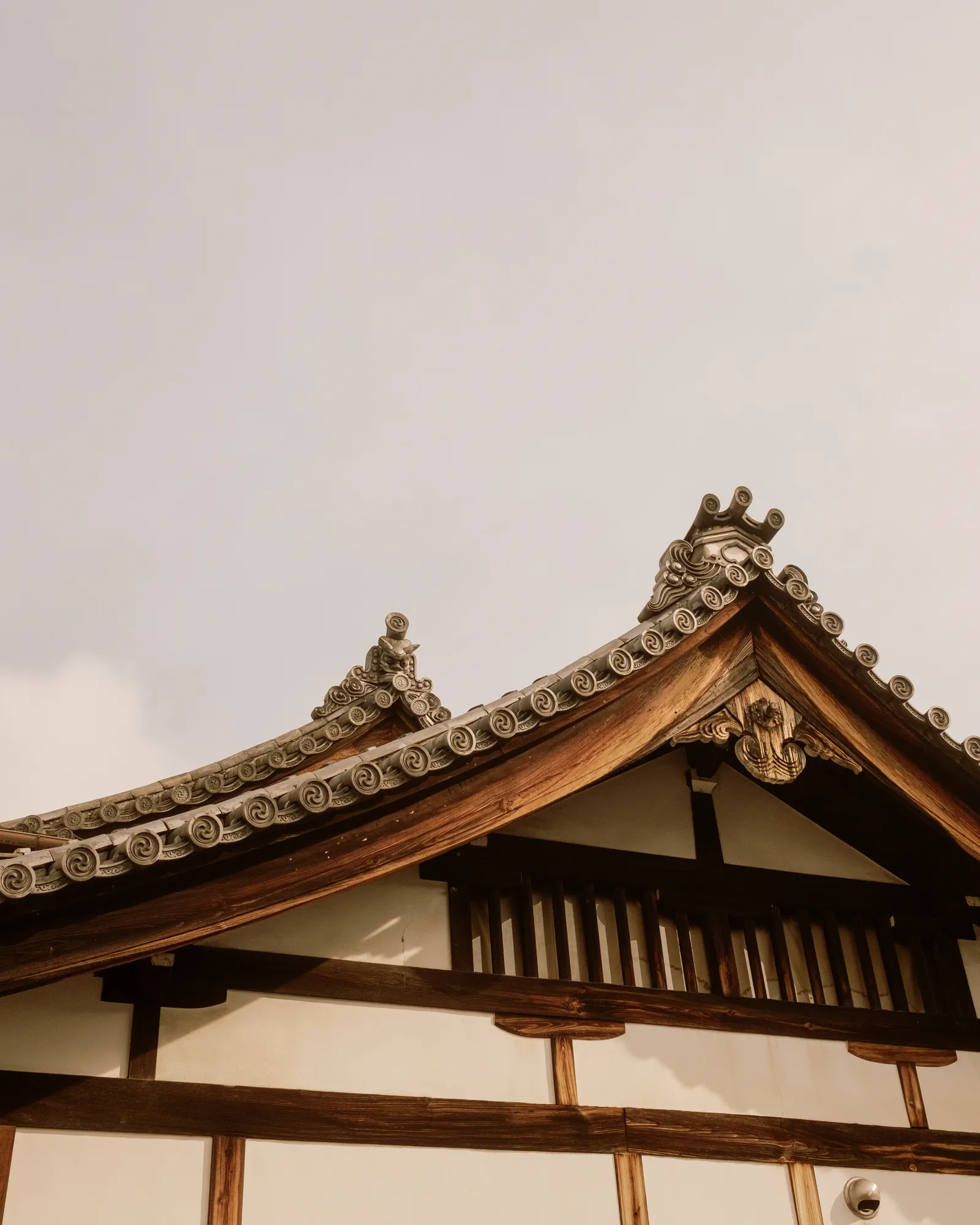 Tiled and timbered temple gable against a pale sky, Kyoto