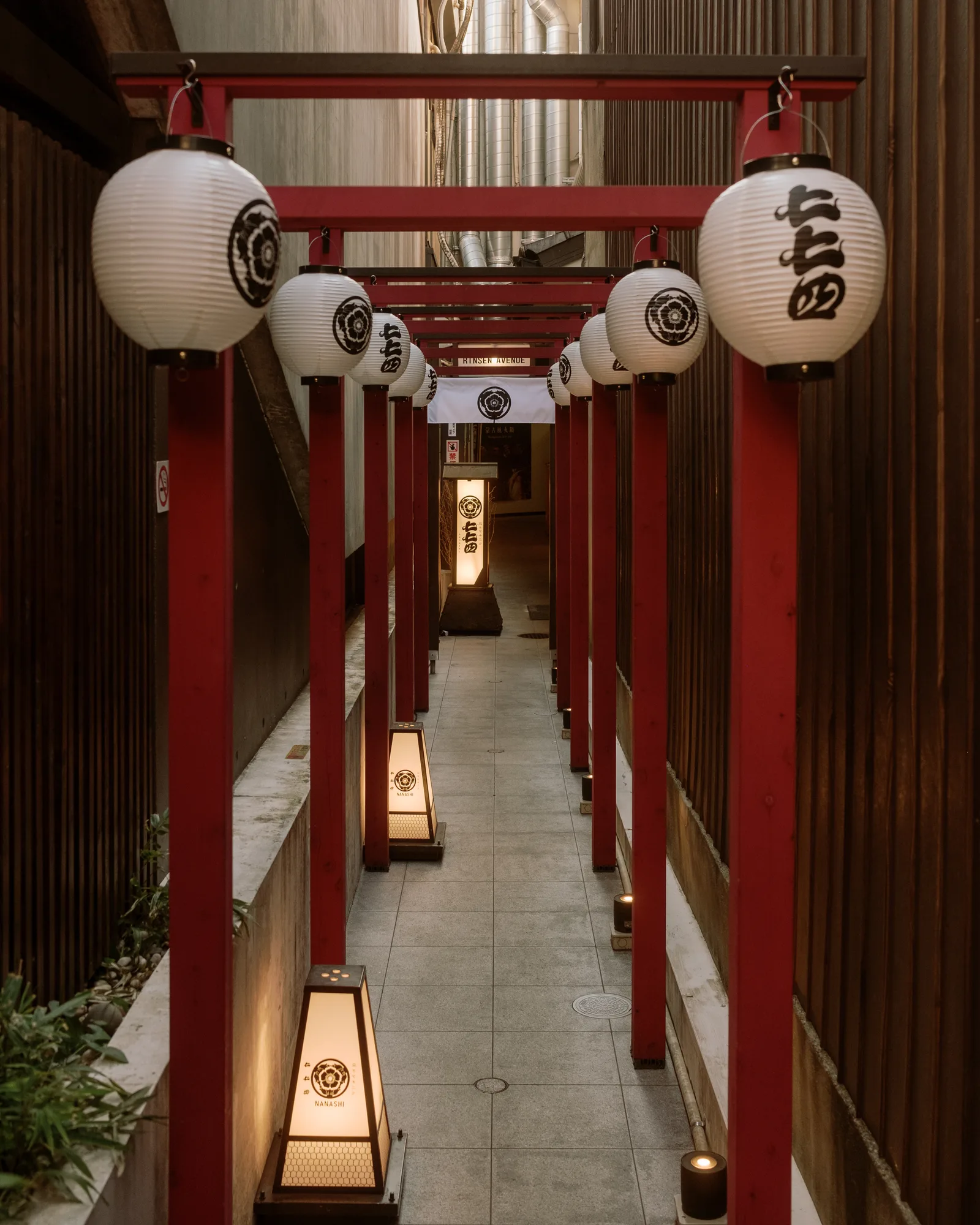 Alley of red torii gates hung with white lanterns and lit floor lamps, Kyoto