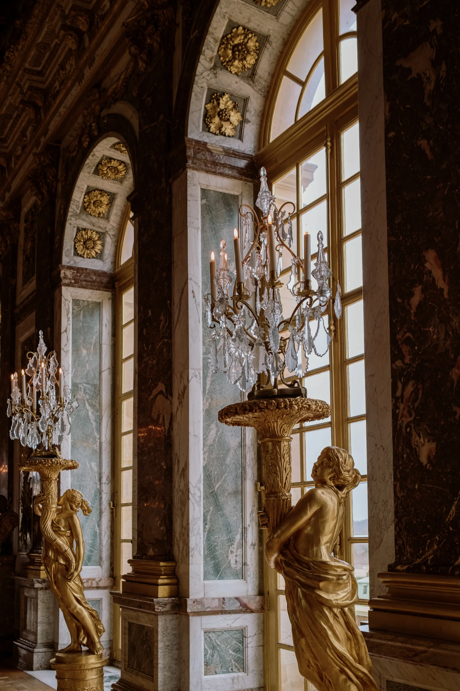 Gilded statues and crystal chandeliers in the Hall of Mirrors at Versailles