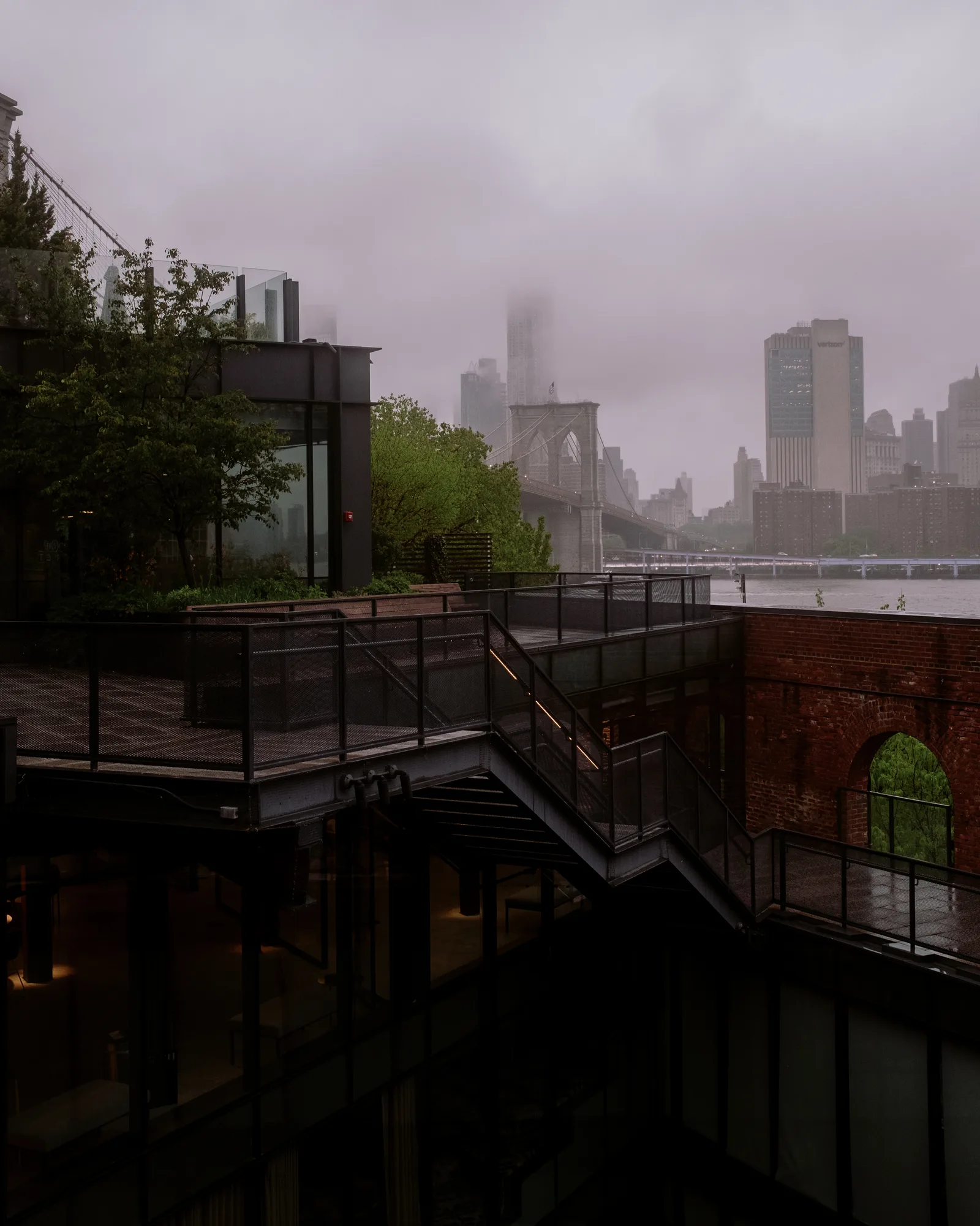 Rooftop terrace with a fogged view toward the Brooklyn Bridge and lower Manhattan