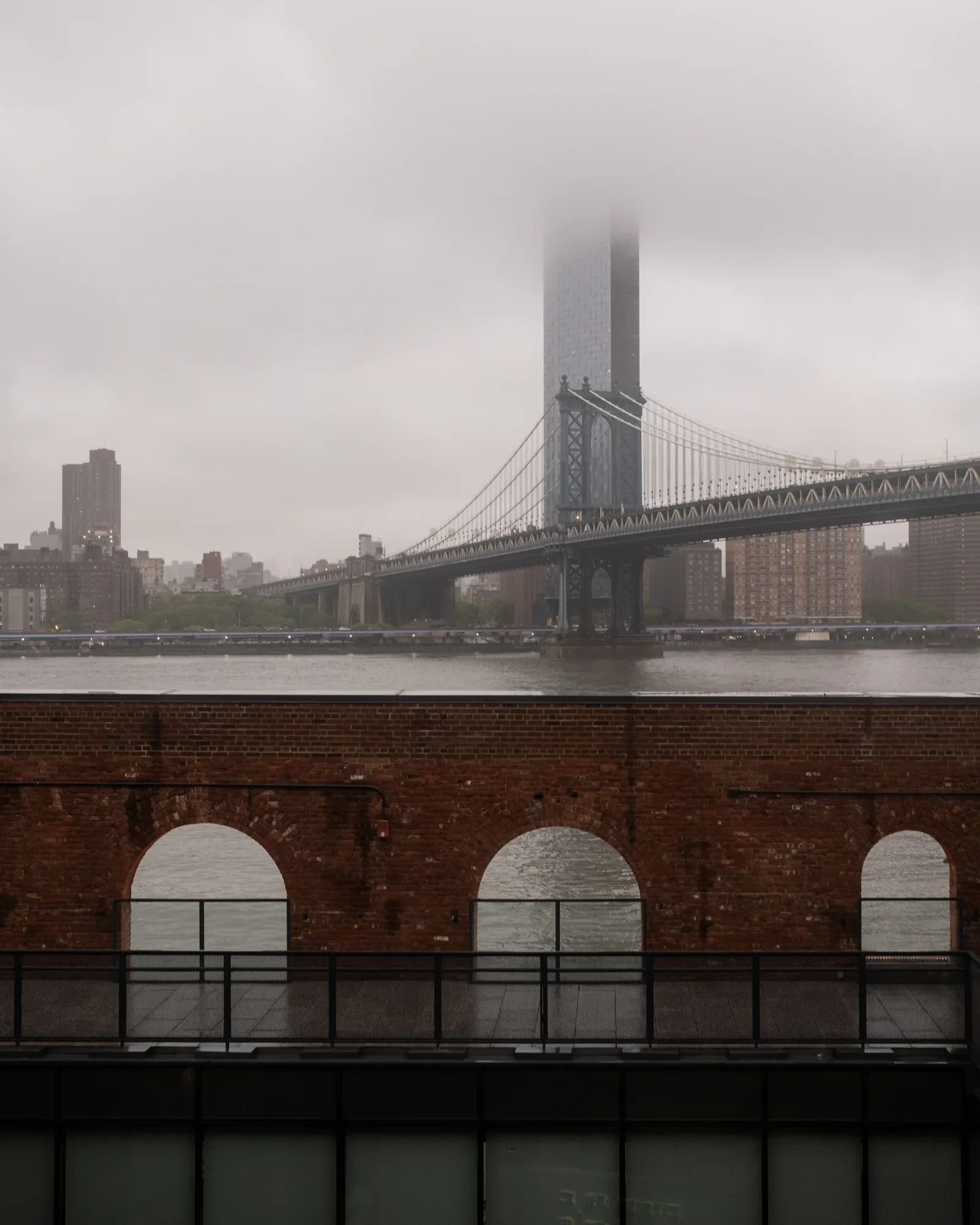 Manhattan Bridge tower vanishing into fog beyond a brick arcade, New York