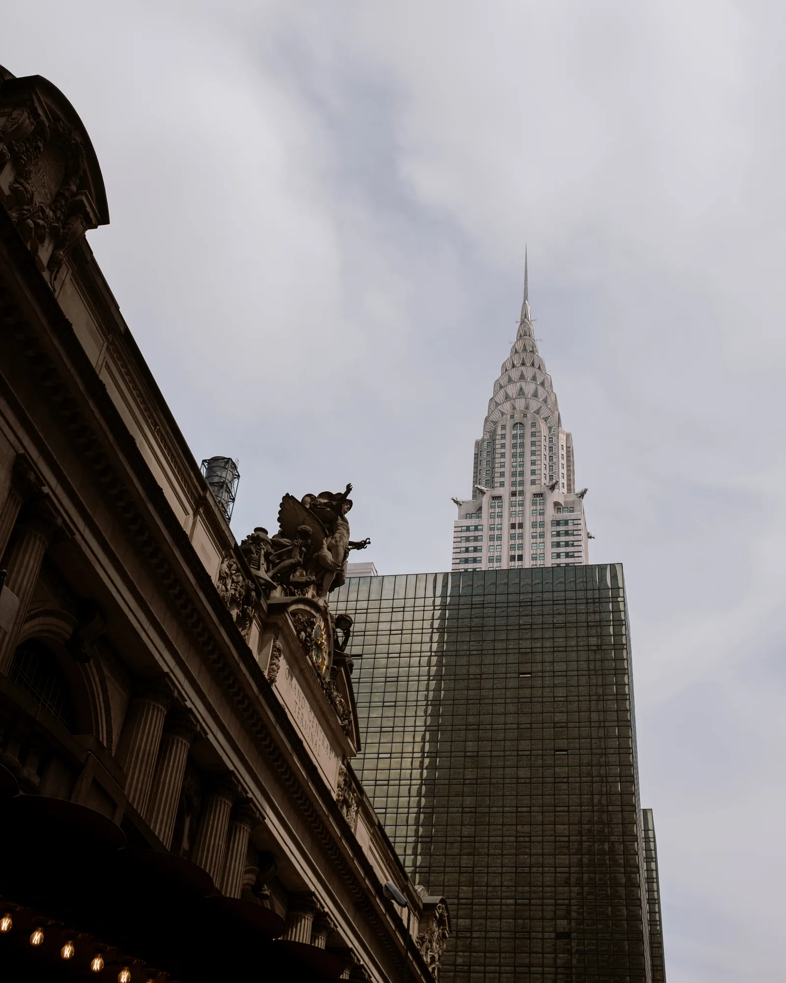 Grand Central's carved facade with the Chrysler Building rising behind a glass tower, New York