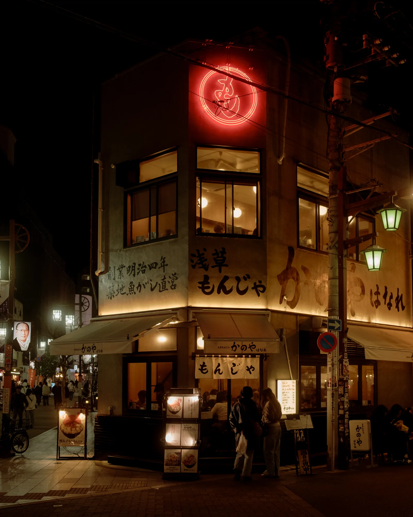 Lit corner restaurant with a red neon sign and diners in Asakusa, Tokyo at night
