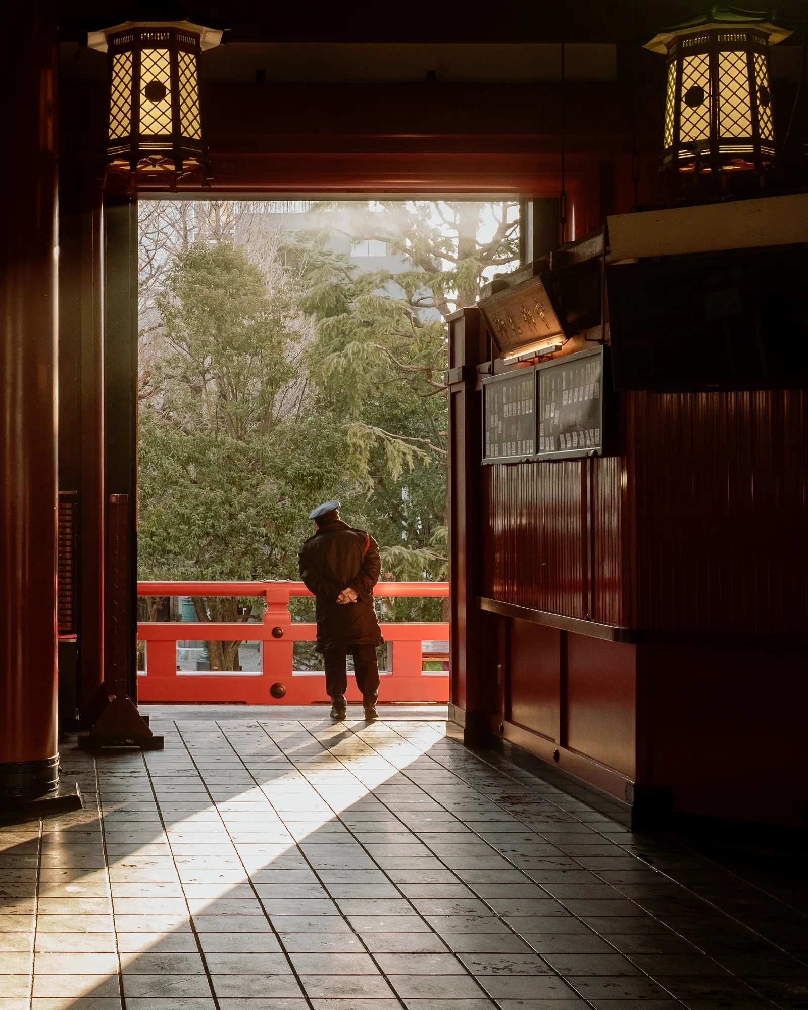 Man standing on a red temple bridge seen through a gate as light falls across the tiled floor, Asakusa, Tokyo