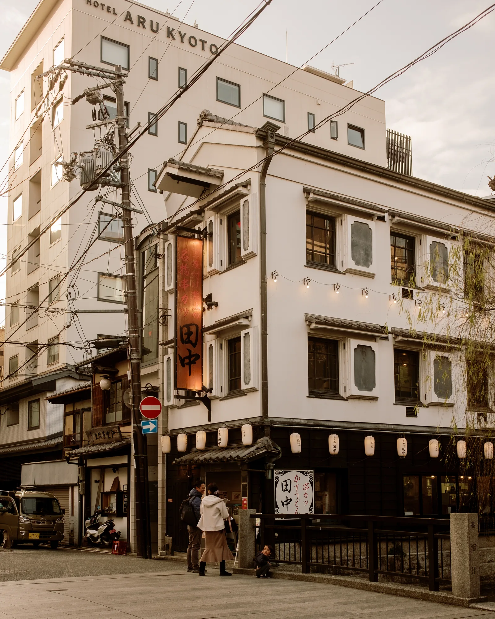 Kyoto corner with a white hotel building, lantern-lined izakaya and pedestrians