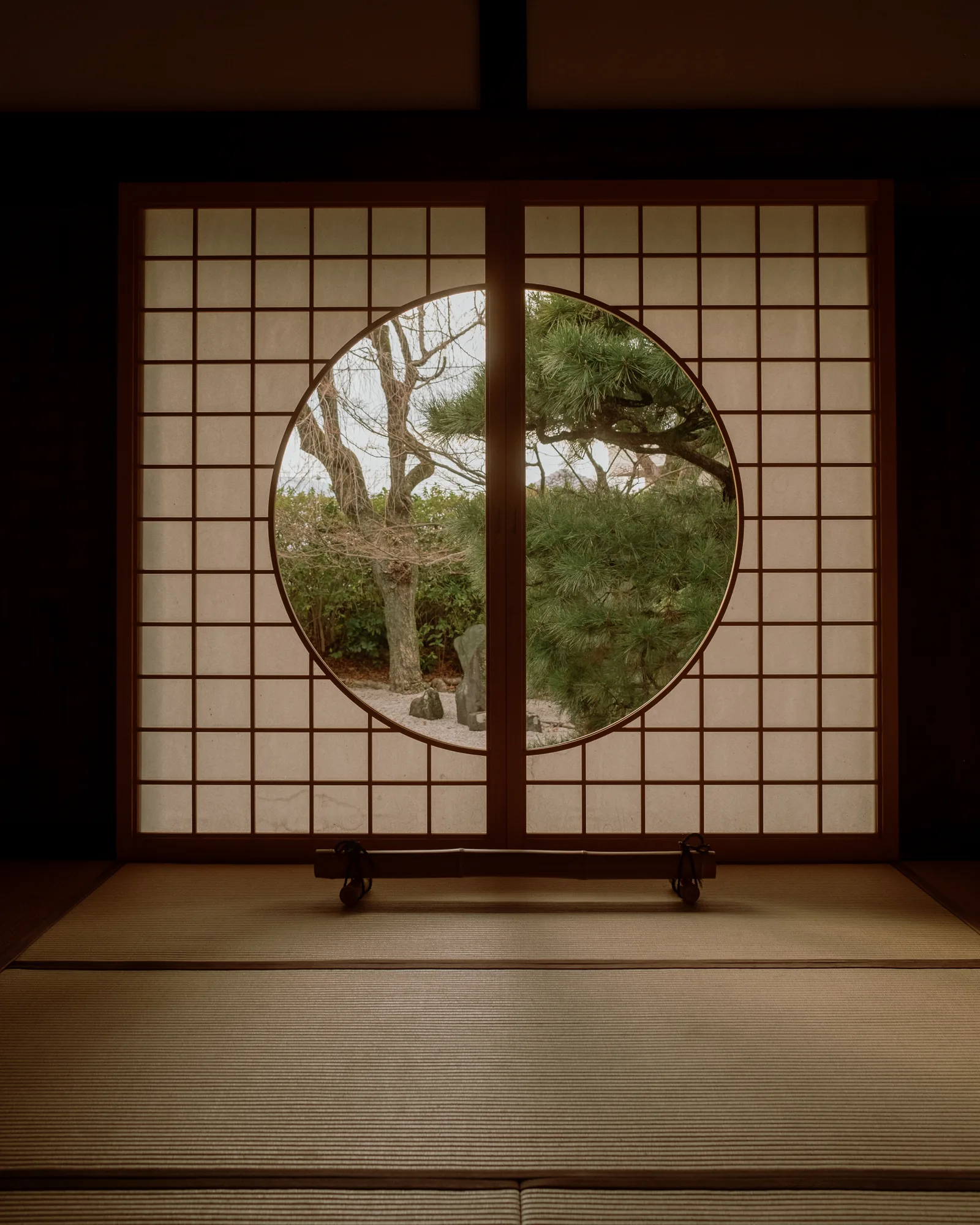 Circular window in a paper screen framing a green garden, seen from a tatami room in Kyoto