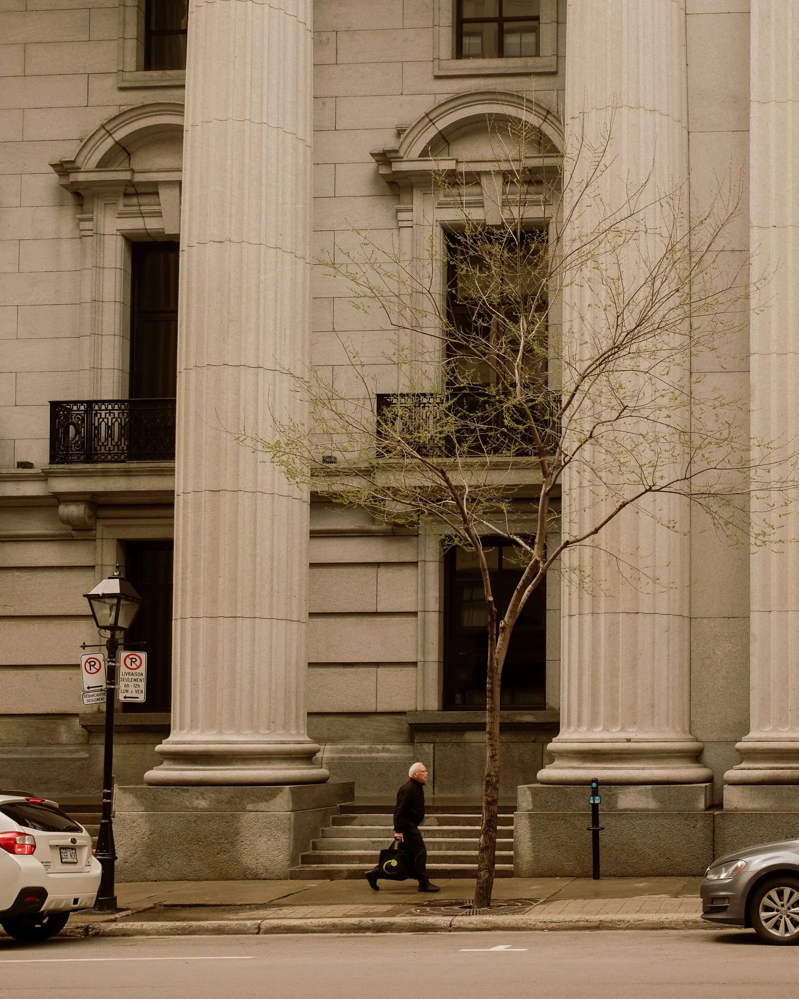 Pedestrian passing the tall stone columns of a classical bank building in Montreal
