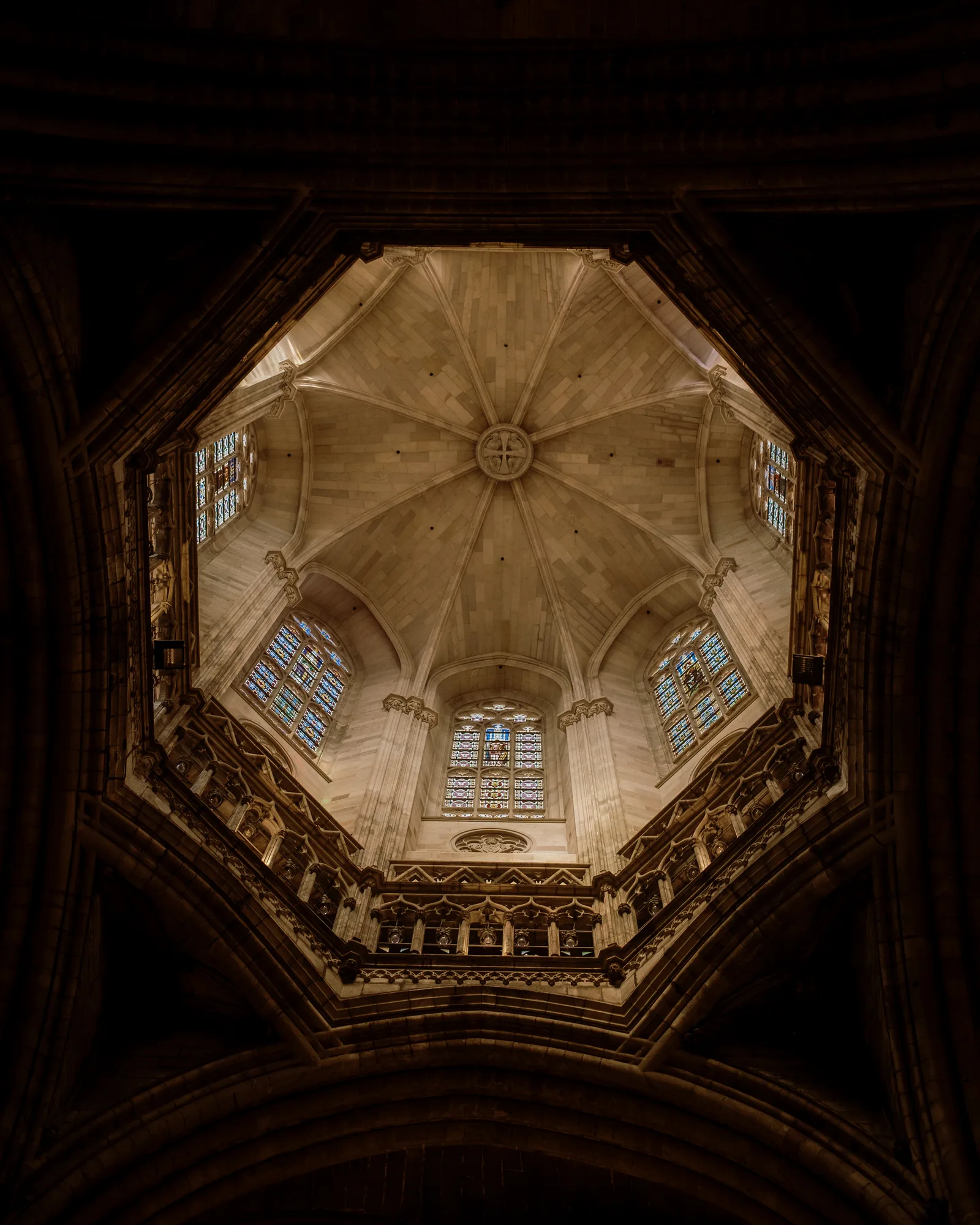 Looking up into an octagonal ribbed dome with stained-glass windows inside a Barcelona church