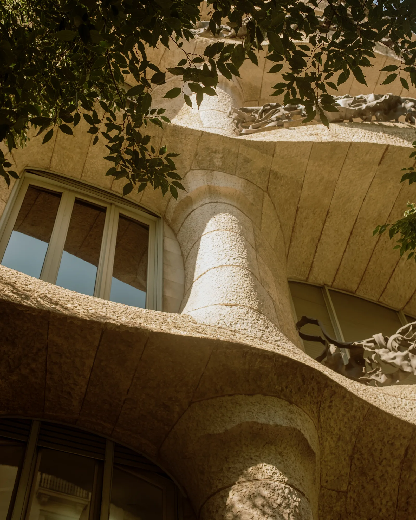 Rounded stone forms and a window corner of Casa Milà seen through leaves, Barcelona