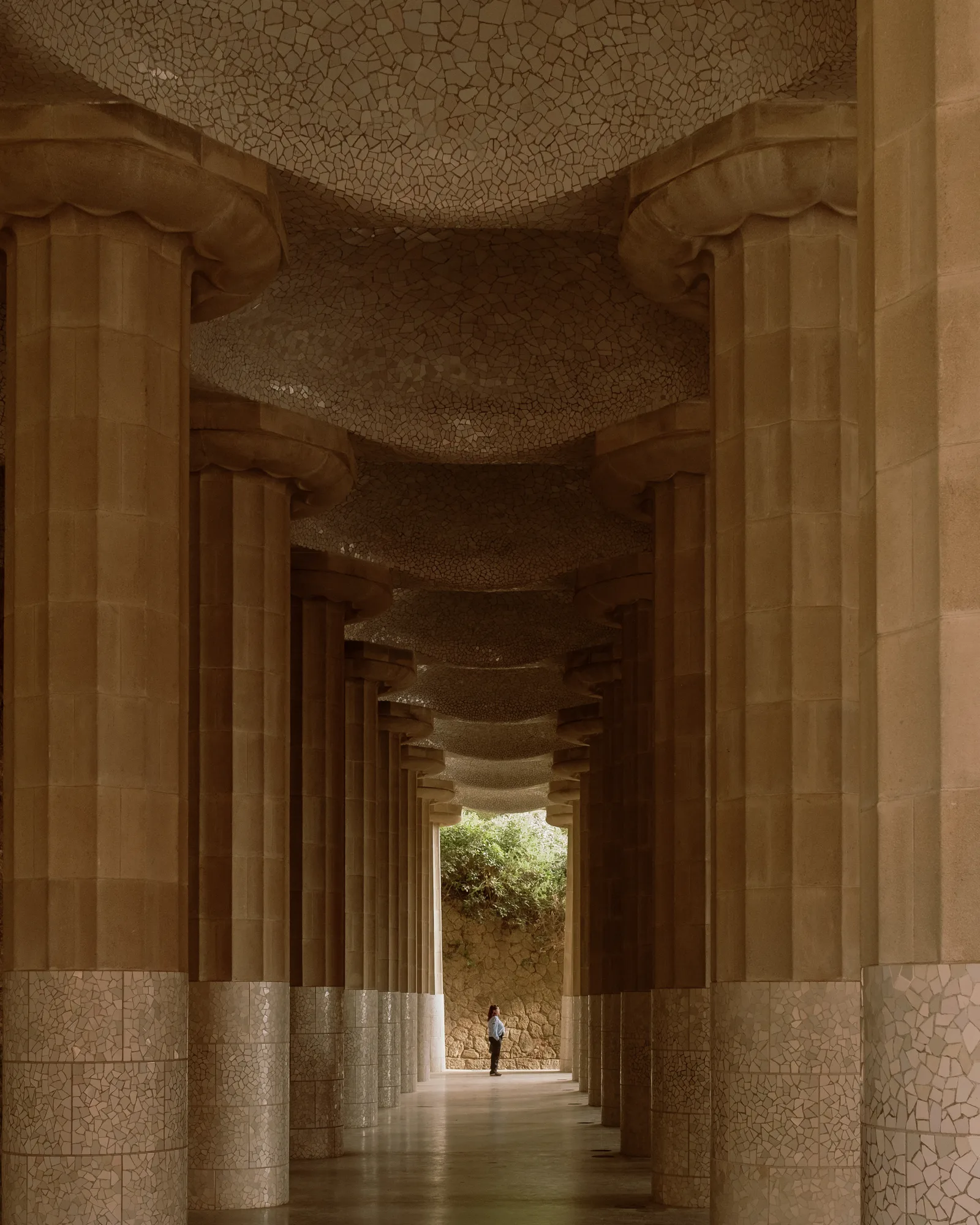 A lone figure at the far end of a stone colonnade in Park Güell, Barcelona