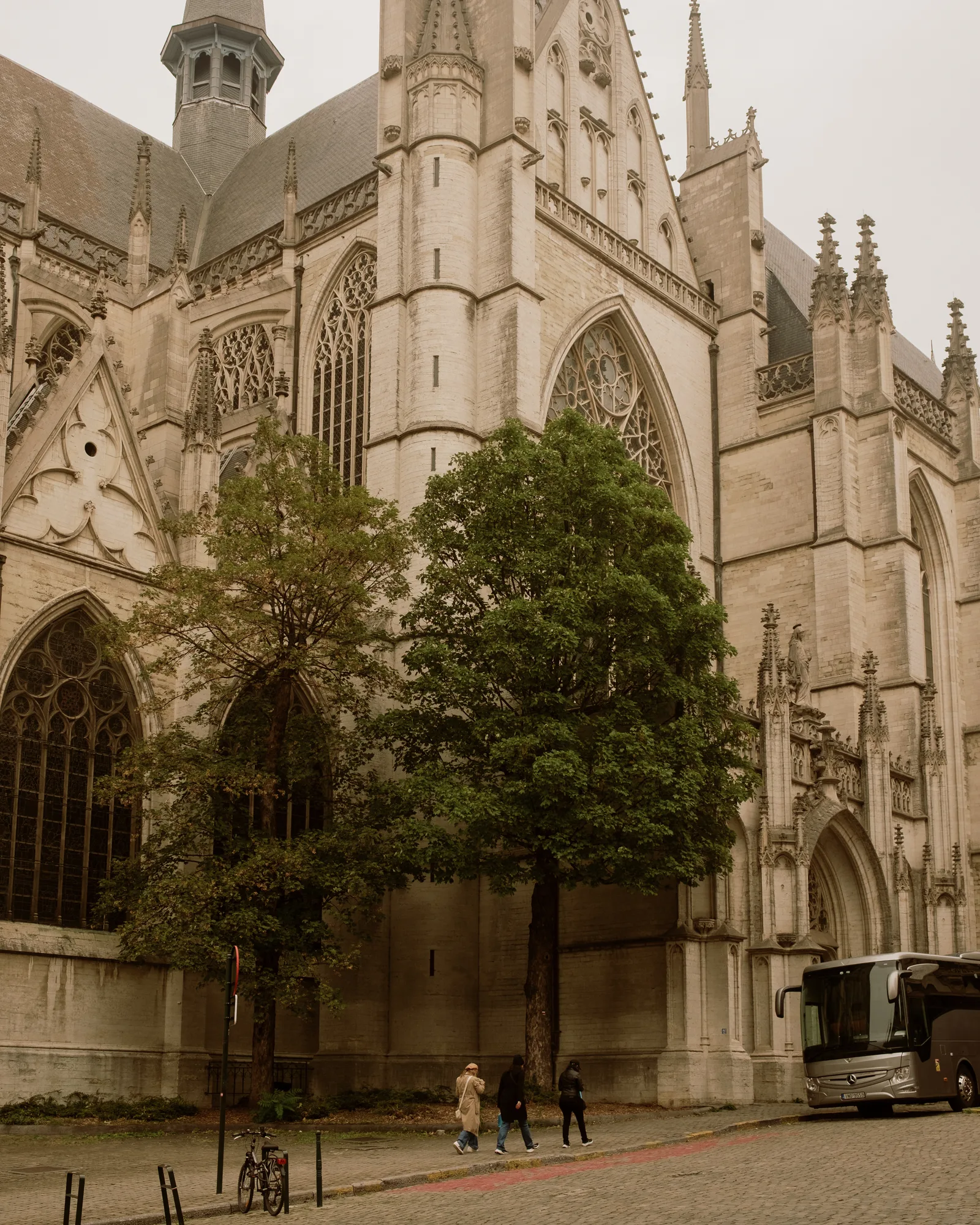 Gothic church with pinnacles rising above trees and a parked bus, Brussels