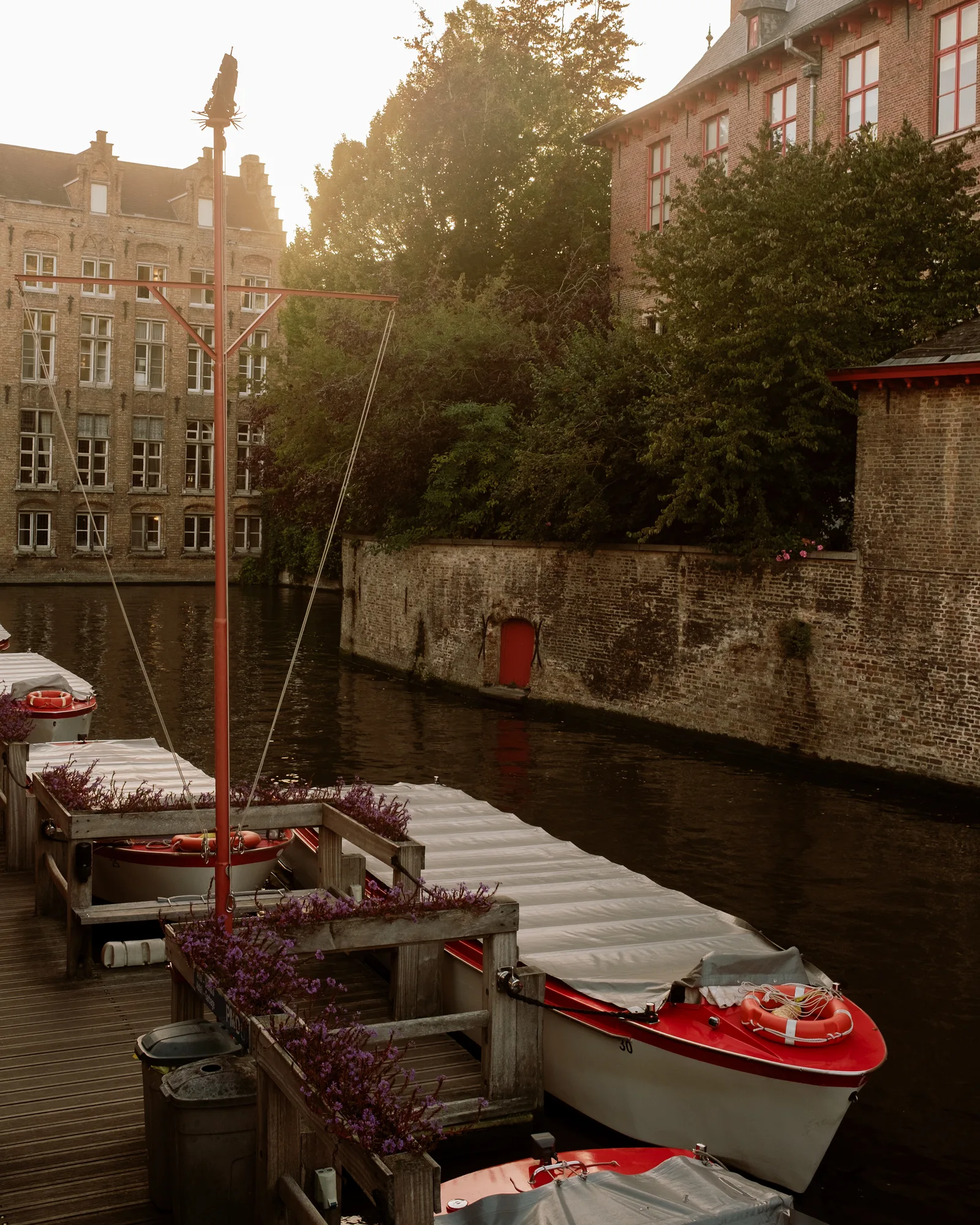 Moored canal boats with red trim and flower boxes beside an old brick wall in Bruges